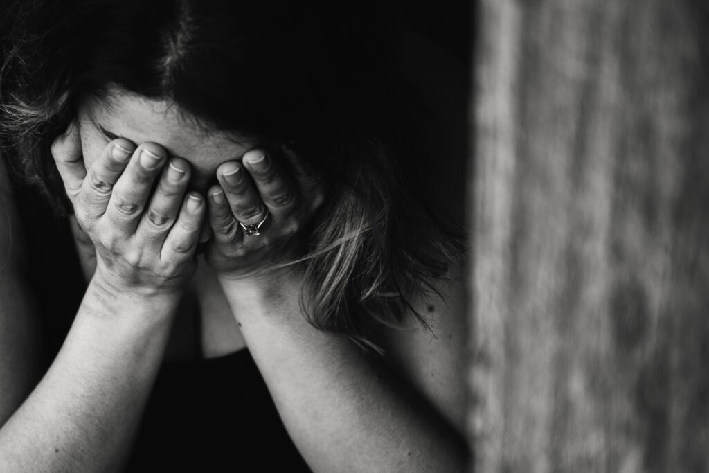 A woman with her hands over her face, feeling anxious or depressed and needing help.